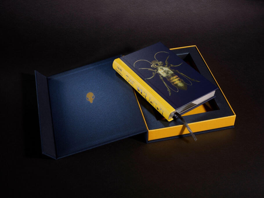 A special edition hardcover of The Wasp Factory by Iain Banks rests partly inside an open presentation box set against a black background.